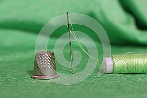 Spool of Green Thread, Thimble and Needle on Green Fabric