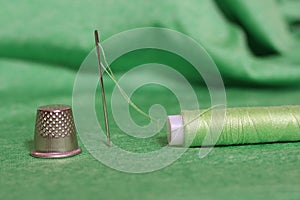 Spool of Green Thread, Thimble and Needle on Green Fabric
