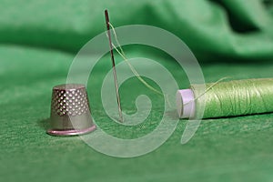 Spool of Green Thread, Thimble and Needle on Green Fabric