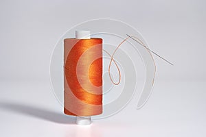 Spool of orange threads with a needle levitate on white background