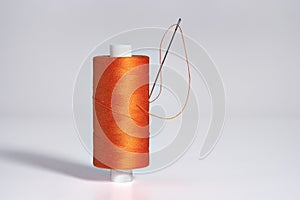 Spool of orange threads  with a needle on white background