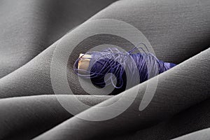 A spool with purple threads in a draped soft gray fabric, close-up, macro. Atelier, tailoring, sewing background. The