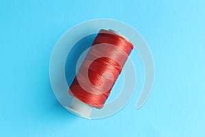 Spool of red sewing thread on light blue background, top view