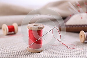 Spool of red sewing thread with needle on fabric