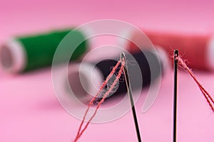 Spool with red thread and needle on pink background