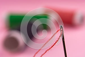 Spool with red thread and needle on pink background