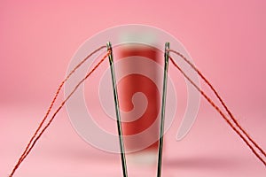 Spool with red thread and needle on pink background