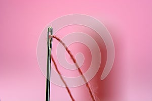 Spool with red thread and needle on pink background