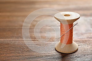 Spool of thread with needle on wooden table. Tailoring equipment
