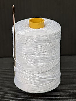 A spool of white thread with a needle isolated on black background