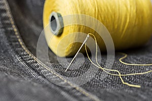 A spool of yellow thread and a needle on dark grey denim.