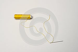 Spool of yellow thread with a needle threaded with thread on a white background