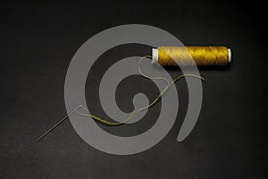 Spool of yellow thread with a threaded needle on a black background