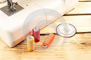 Spools of colored thread, sewing pins next to a sewing machine on a wooden background