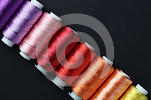 Spools of colorful sewing threads on black background, flat lay