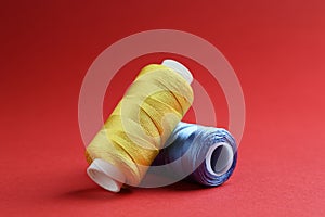 Spools of colorful sewing threads on red background, closeup