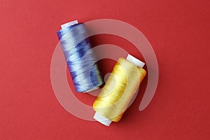Spools of colorful sewing threads on red background, flat lay
