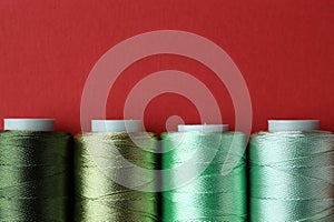 Spools of colorful sewing threads on red background, flat lay. Space for text copy