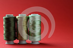 Spools of colorful sewing threads on red background, space for text