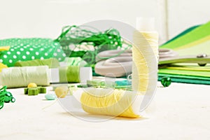 Spools of thread, fabrics and accessories for sewing on a light background shades of green and yellow