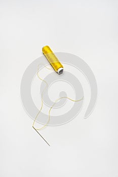 Spools of yellow thread with a needle threaded with thread of the same color on a white background