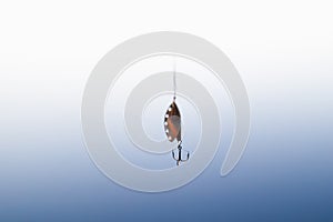 Spoon-bait on a fishing line, blue water background