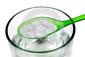 Spoon of baking soda over glass of water, isolated on white backgrpnd
