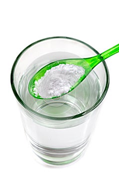 Spoon of baking soda over glass of water, isolated on white backgrpnd