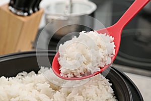 Spoon with boiled rice over cooker against blurred background