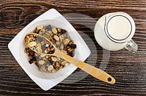 Spoon in bowl with cereal breakfast with peanut and raisin, pitcher with yogurt on wooden table. Top view