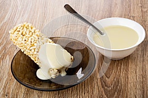 Spoon in bowl with condensed milk, milk poured on briquette of puffed rice in saucer on table