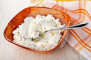 Spoon in bowl with defatted cottage cheese, napkin on wooden table