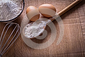 Spoon bowl with flour eggs corolla on wooden board
