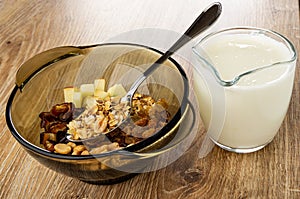 Spoon in bowl with ingredients for muesli. pitcher with yogurt on wooden table