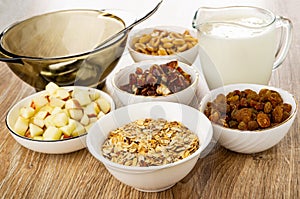 Spoon in bowl, ingredients for muesli in white bowls, yogurt in transparent jug on table