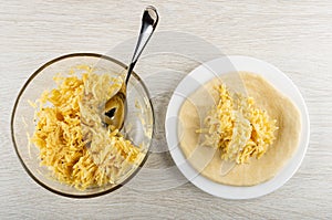 Spoon in bowl with mix of grated cheese and egg, flatbread with cheese in plate on wooden table. Top view