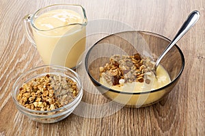 Spoon in bowl with muesli and yogurt, jug of yogurt, bowl with granola on table