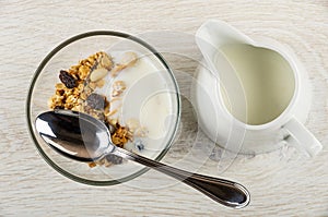 Spoon in bowl with muesli and yogurt, pitcher with yogurt on table. Top view