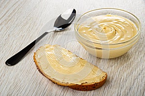 Spoon, bowl with peanut paste, sandwich with peanut butter on wooden table