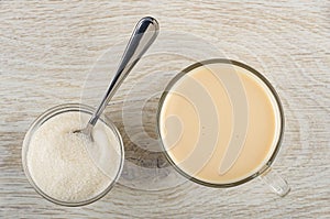 Spoon in bowl with sugar, cup with fermented baked milk on wooden table. Top view