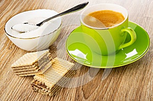 Spoon in bowl with sugar, halves of wafer with chocolate, coffee espresso in cup on saucer on wooden table