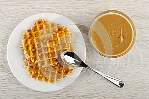 Spoon on bowl with waffle, bowl with peanut butter on wooden table. Top view