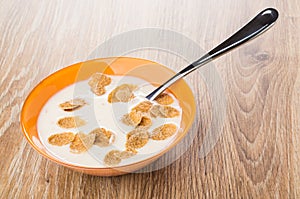Spoon in bowl with yogurt, multicereal flakes on wooden table