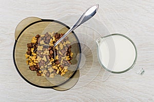 Spoon with breakfast cereals in bowl, jug of yogurt