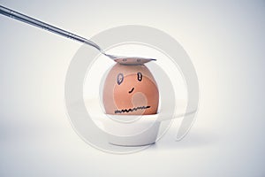 Spoon breaks sad egg on a stand in the form of human head .