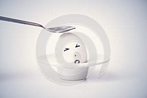 Spoon breaks sad egg on a stand in the form of human head .