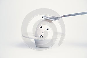 Spoon breaks sad egg on a stand in the form of human head .