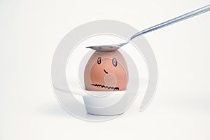 Spoon breaks sad egg on a stand in the form of human head .