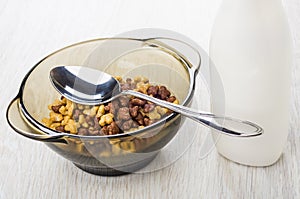 Spoon in brown bowl with breakfast cereals, bottle of yogurt