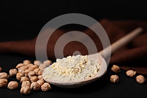 Spoon with chickpea flour and seeds on black table, closeup. Space for text